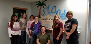 Group of women standing in front of sign saying "Island Escape Room" with owner