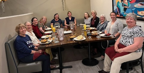 A dozen or so women seated around a large, rectangular table looking at the camera.